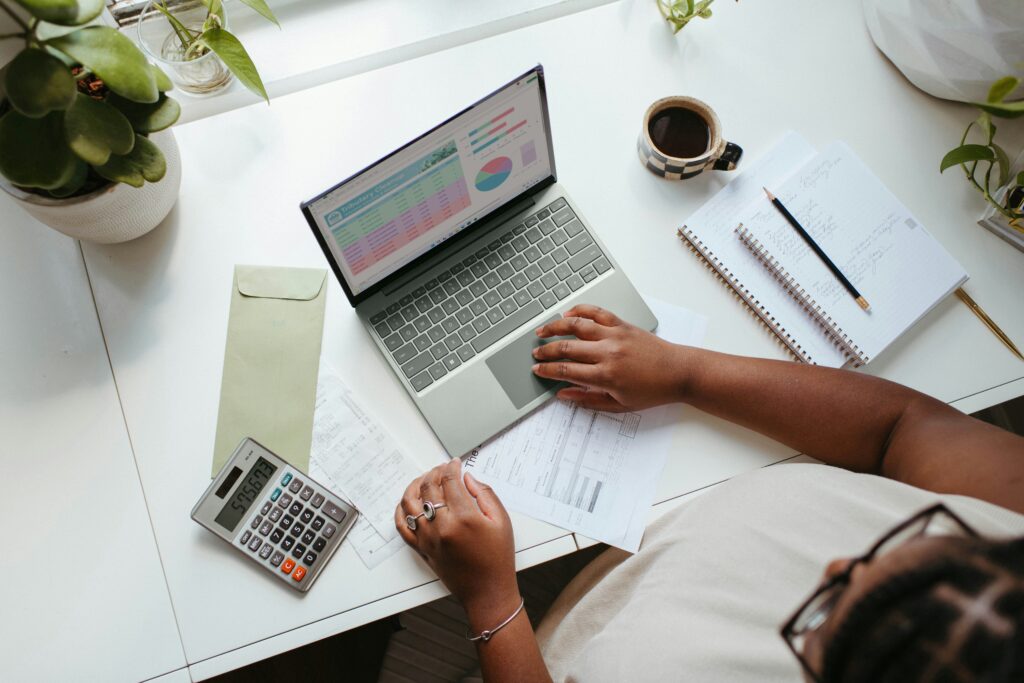 Vue du dessus où l'on voit une personne travailler sur un ordinateur avec à côté une calculatrice et un carnet de notes